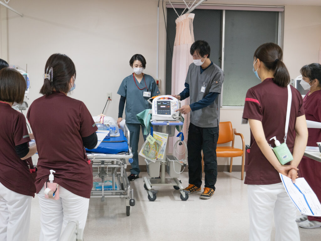 病院内でストレッチャーと医療機器のそばに立つスタッフ