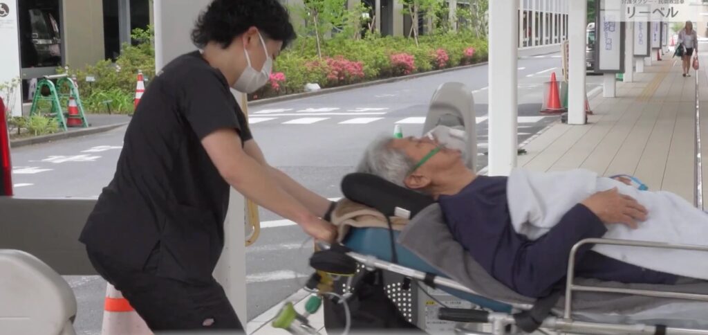 鼻から酸素を吸いながらストレッチャーで移動する方と、付き添うリーベルのスタッフ