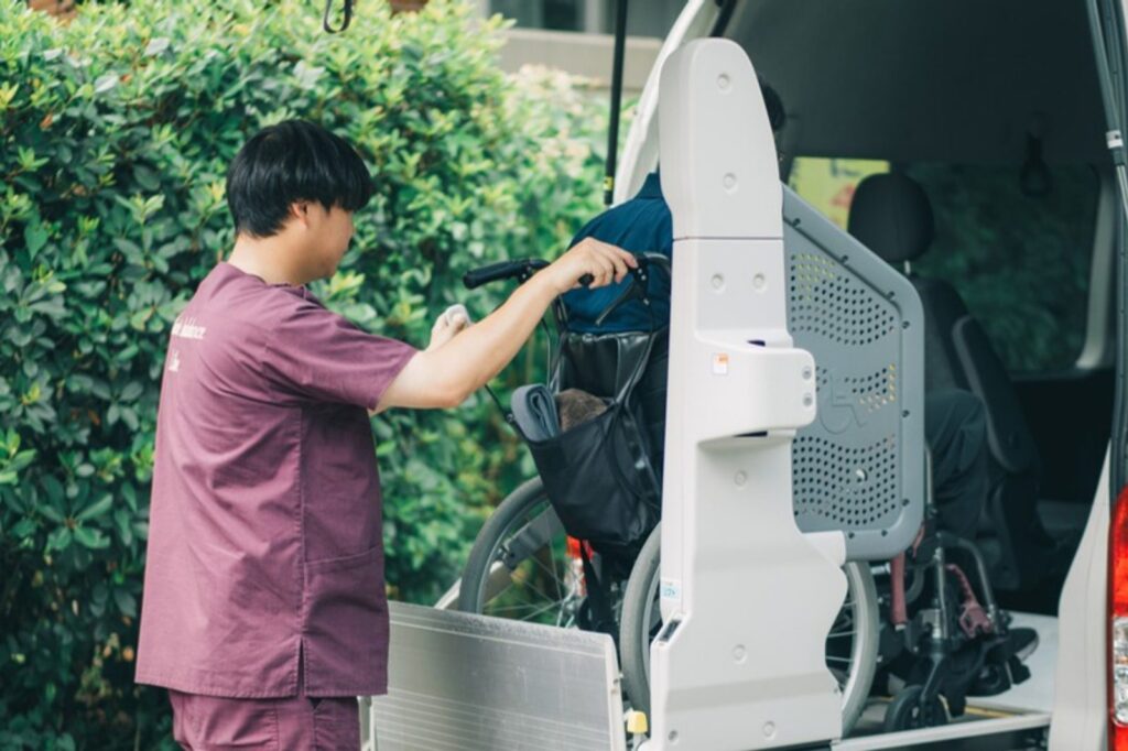 車両の後部で車いすを固定するスタッフ(介助の一例)